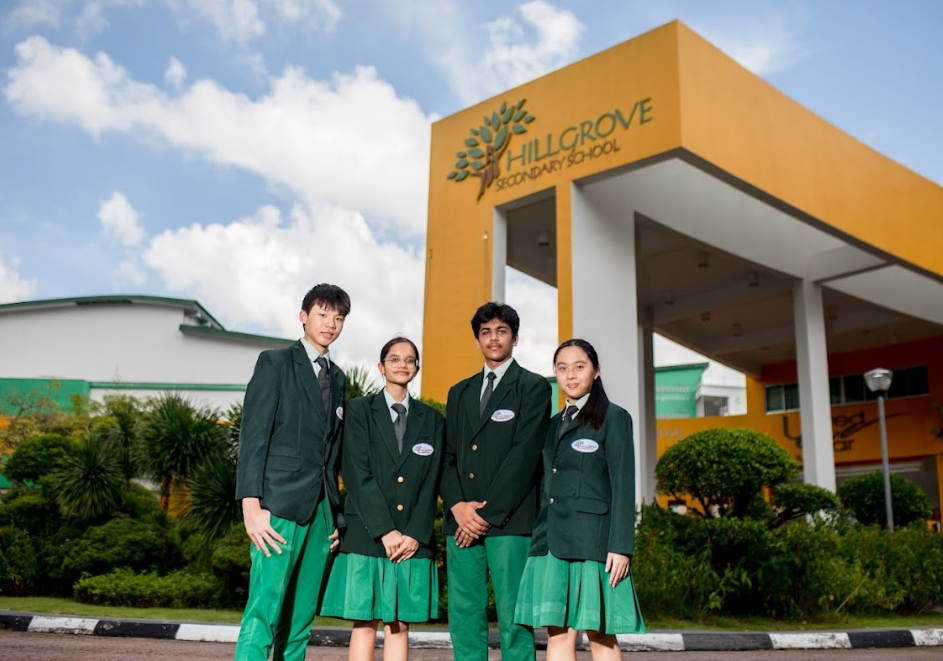 Four students in green uniforms stand outside Hillgrove Secondary School under an orange entrance arch.